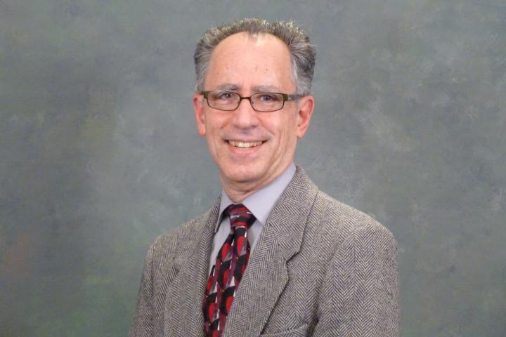 Hal Luft smiling in gray suit with red tie and gray background